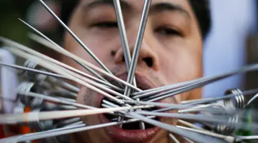 Seorang pemuja dari Kuil Samkong menusukkan besi ke pipi saat memeriahkan festival vegetarian di Phuket, Thailand (4/10). Festival ini menampilkan aksi ekstrem pemuja dengan menusukkan benda tajam ke wajah. (REUTERS/Jorge Silva)