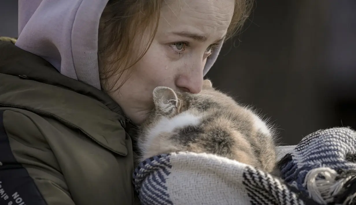 Seorang wanita yang dievakuasi dari Irpin menangis mencium kucing yang dibungkus selimut di titik triase di Kyiv, Ukraina, 11 Maret 2022. Dalam eksodus lebih dari 2,5 juta orang yang melarikan diri dari invasi Rusia, terdapat hewan peliharaan yang tidak dapat ditinggalkan. (AP Photo/Vadim Ghirda)