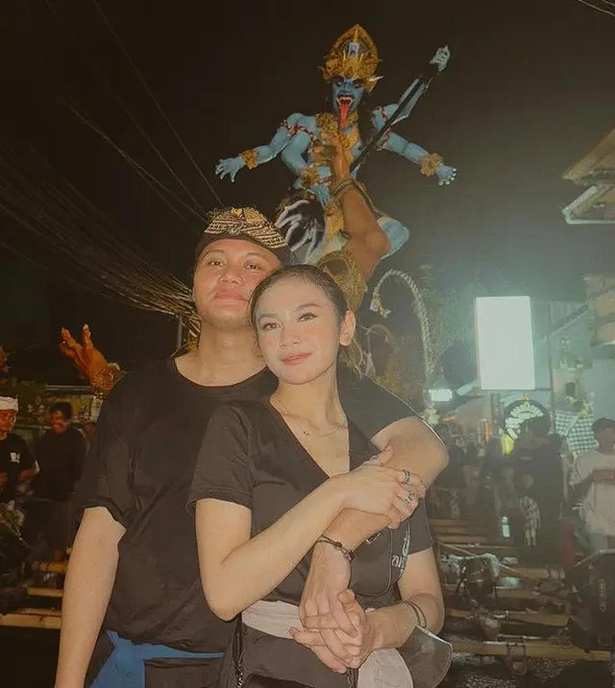 Rizky Febian, bersama kekasihnya, mempesona dalam pawai ogoh-ogoh dengan paduan kaos hitam, kain biru di pinggang, dan hiasan kepala.&nbsp;