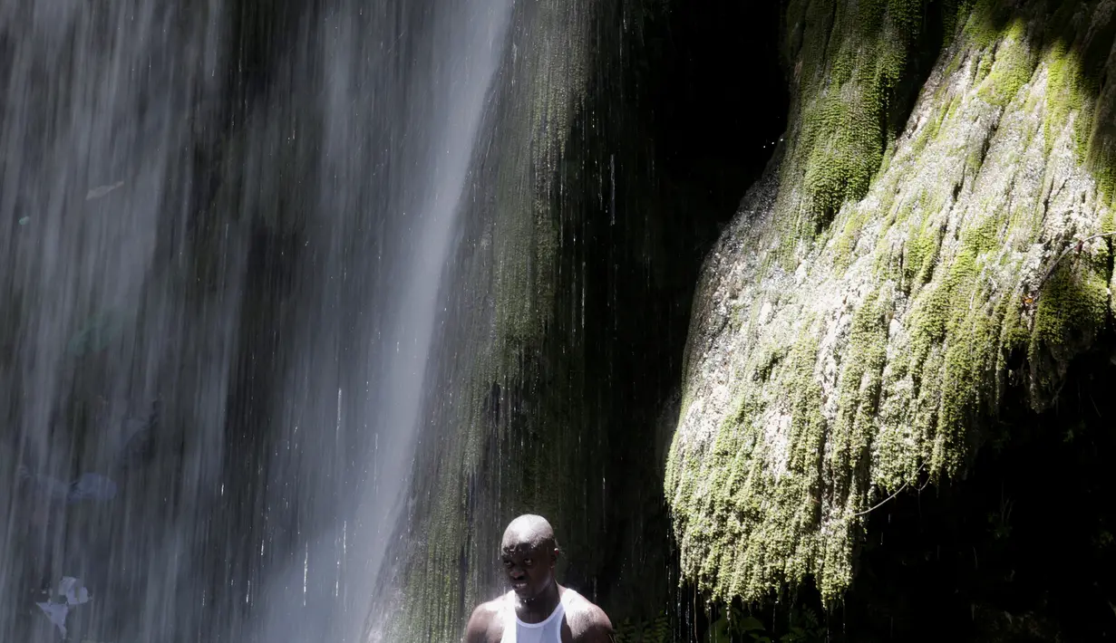 Seorang peziarah mandi di bawah air terjun di Saut d' Eau, Haiti, (16/7). Mereka merupakan penganut aliran Voodoo menggelar ritual mandi suci di air terjun Saut D'Eau. (REUTERS/Andres Martinez Casares)