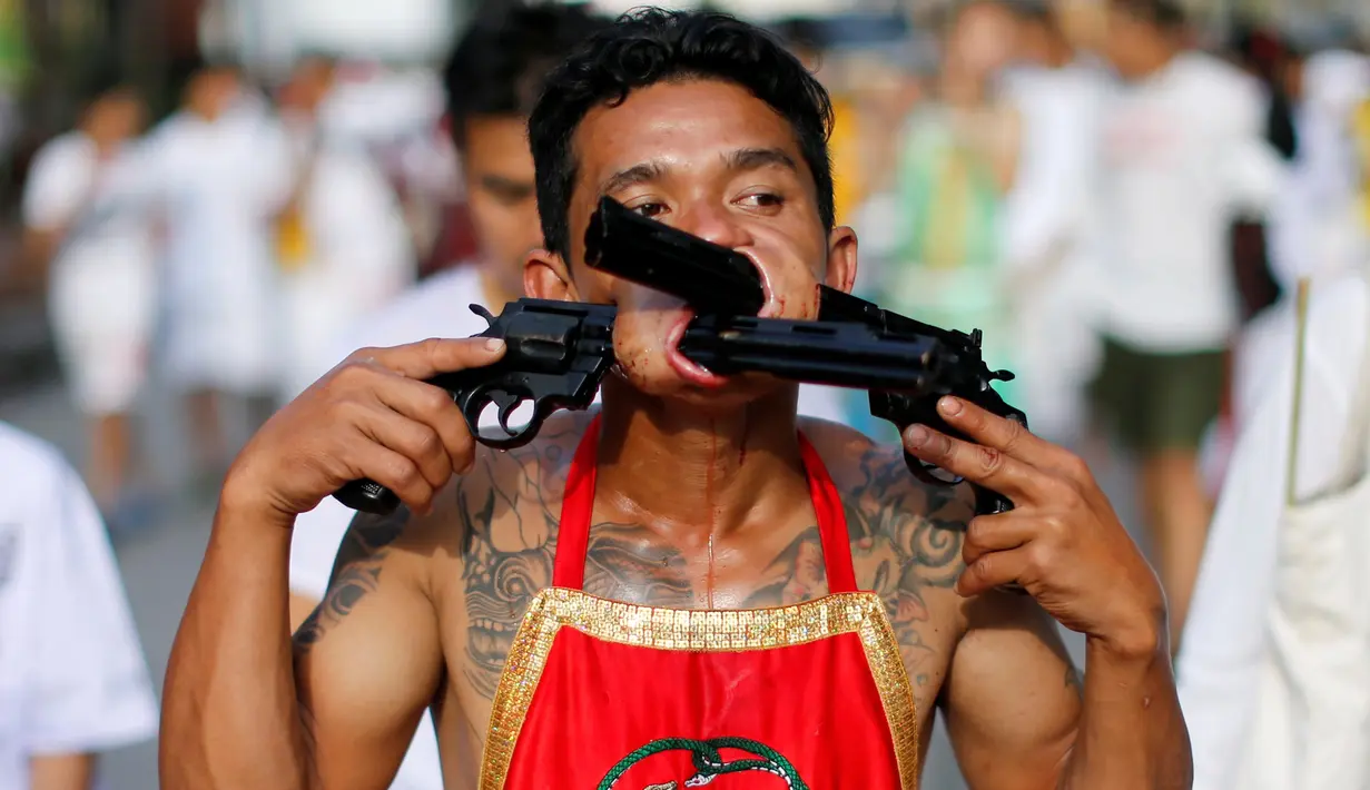 Seorang pemuja dari Kuil Samkong menusukkan dua revolver pada pipinya saat beratraksi dalam Festival Vegetarian di Phuket, Thailand, Selasa (4/10). Festival ini menampilkan aksi ekstrem pemuja dengan menusukkan benda tajam ke wajah. (REUTERS/Jorge Silva)