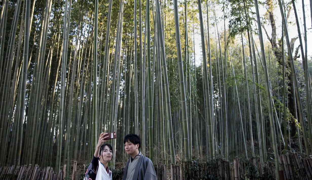 Wisatawan mengenakan kimono sambil berswafoto saat mengunjungi Hutan Bambu Sagano di Arashiyama, Kyoto pada 8 Desember 2018. Karena keindahan hutan bambunya, membuat kawasan wisata ini menjadi sangat terkenal di Jepang. (Behrouz MEHRI / AFP)