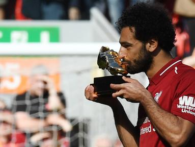 Mohamed Salah mencium penghargaan Sepatu Emas yang diraihnya setelah Liverpool menekuk Brighton and Hove Albion di Anfield, Minggu (13/5). Salah merebut Sepatu Emas atas keberhasilannya menjadi top scorer Premier League musim ini. (AFP/Paul ELLIS)