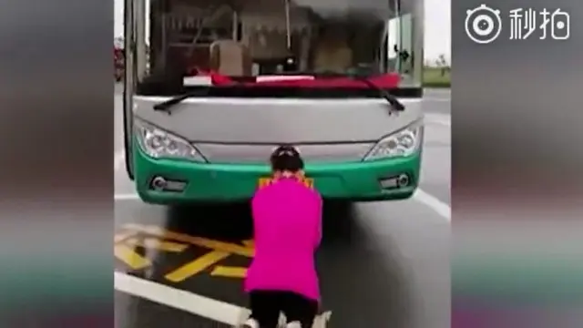 Wanita berlutut di depan bus.