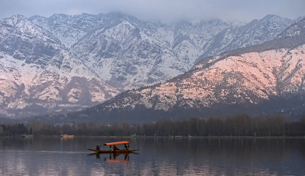 Orang-orang menikmati perjalanan dengan perahu dengan latar belakang pegunungan yang tertutup salju di danau Dal di Srinagar (11/1/2022). Danau Dal yang merupakan danau terbesar kedua di propinsi Jammu dan Kashmir negara bagian India ini merupakan pusat pariwisata dan rekreasi. (AFP/Tauseef Mustafa)