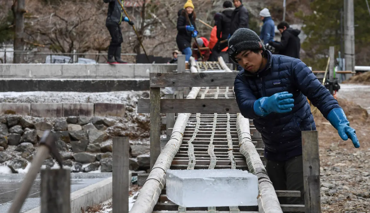 Seorang pekerja menggeser balok es alami untuk membuat kakigori atau es serut di atas rel bambu setelah dipotong dari kolam terbuka di pabrik di Nikko, Prefektur Tochigi (10/1/2019). (AFP Photo/Toshifumi Kitamura)