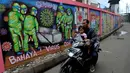 Pengendara sepeda motor melintasi mural bertema COVID-19 di kawasan Tanah Tinggi, Tangerang, Banten, Rabu (20/1/2020). Kegiatan ini dalam rangka mensosialisasikan bahaya penyebaran COVID-19 kepada warga pengguna jalan umum. (merdeka.com/Arie Basuki)