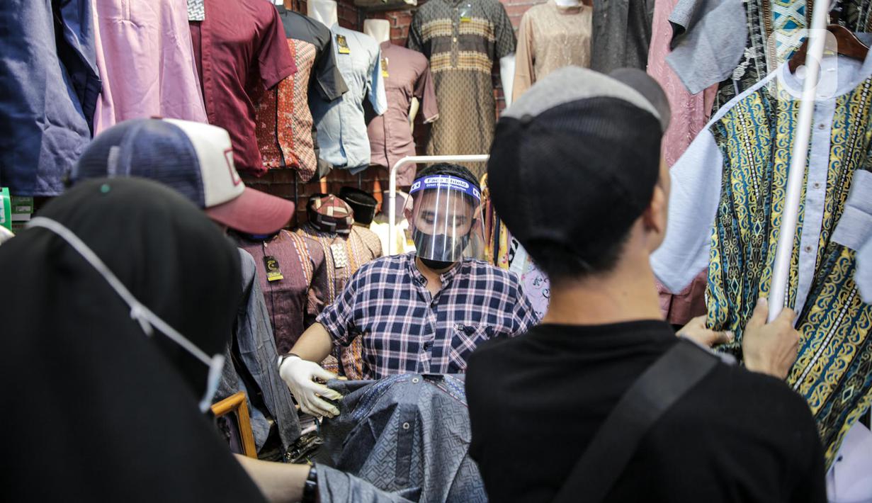 Pedagang menggunakan alat pelindung wajah (Face Shield) saat melayani pembeli di Kawasan Tanah Abang, Jakarta, Senin (18/5/2020). Penggunaan alat pelindung wajah itu sebagai upaya untuk melindungi diri saat berhubungan dengan pembeli dalam pecegahan penyebaran COVID-19. (Liputan6.com/Faizal Fanani)