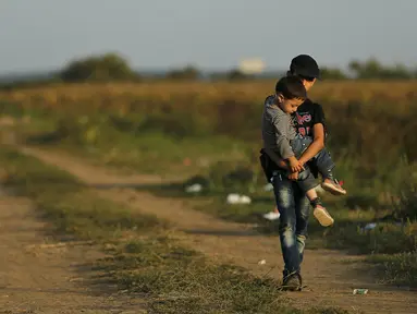 Seorang imigran remaja menggendong adiknya melintasi perbatasan dari Serbia ke Kroasia di Tovarnik (18/9/2015). (REUTERS / Antonio Bronic)