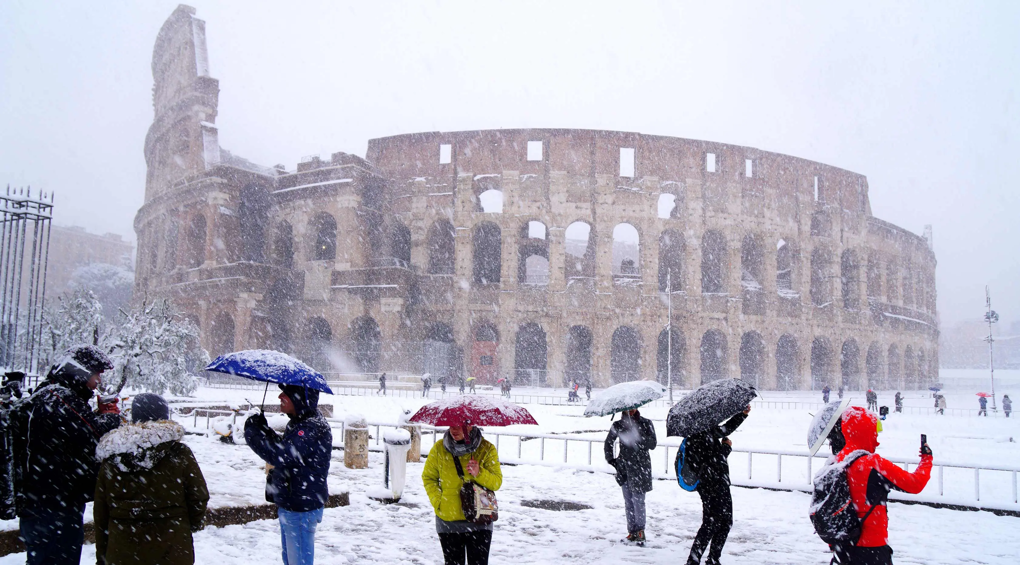 Sejumlah wisatawan mengabadikan Colosseum kuno saat hujan salju di Roma, Italia (26/2). (AFP Photo/Vicenzo Pinto)