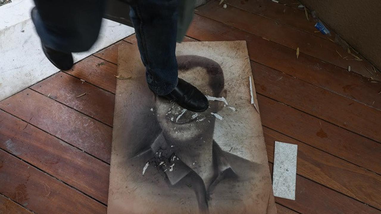 Seorang pria menginjak gambar presiden terguling, Bashar al-Assad, saat orang-orang memasuki kediamannya di daerah Malki, Damaskus, pada Minggu (8/12/2024), setelah pemberontak menyatakan mereka telah merebut ibu kota Suriah.