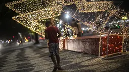 Seorang anak berjalan di sepanjang trotoar pantai Copacabana dengan latar belakang lampu Natal, di Rio de Janeiro, Brasil (11/12/2021). Jelang perayaan Natal, taman dan pantai dihiasi lampu-lampu yang indah. (AP Photo/Bruna Prado)