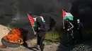 Demonstran berlari sambil mengibarkan bendera nasional mereka sementara yang lain membakar ban saat protes terhadap serangan militer Israel ke Kota Nablus, Tepi Barat, di sepanjang pagar perbatasan dengan Israel di sebelah timur Kota Gaza, 22 Februari 2023. Para pejabat Palestina mengatakan sejumlah warga Palestina telah terbunuh dan lebih dari seratus orang terluka dalam serangan tentara Israel yang jarang terjadi di Tepi Barat. (AP Photo/Adel Hana)