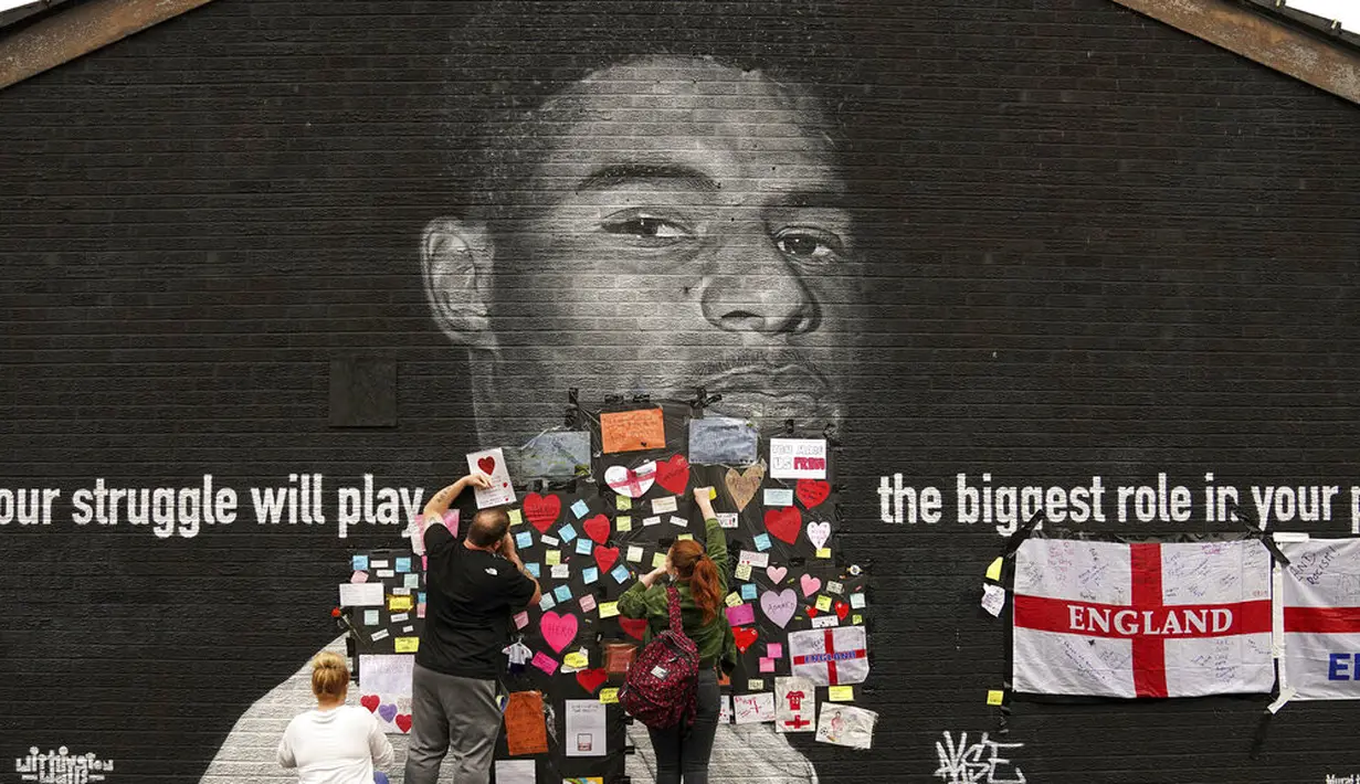 Orang-orang menempatkan pesan dukungan di mural Marcus Rashford yang dirusak di Withington, Manchester (12/7/2021). PM Inggris Boris Johnson mengutuk pelecehan rasis kepada tiga pemain Black England yang gagal mengeksekusi penalti melawan Italia di final Euro 2020. (Peter Byrne/PA via AP)