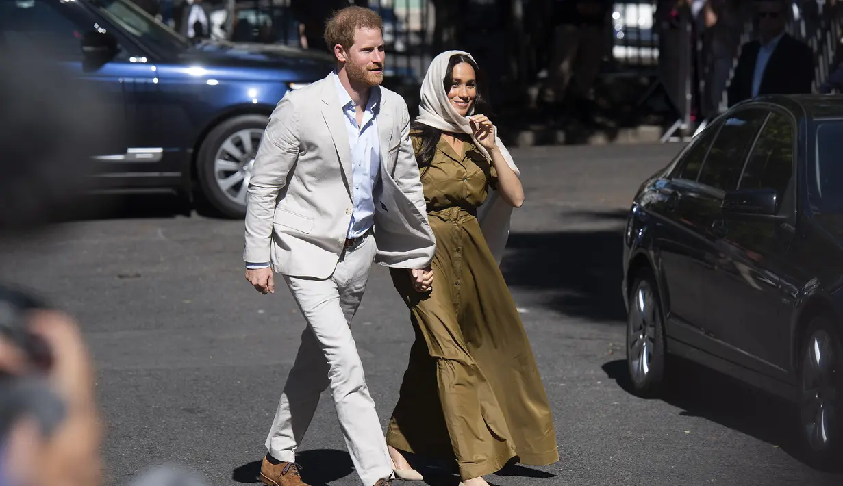 Duchess of Sussex Meghan Markle menggandeng tangan suaminya, Pangeran Harry saat tiba di Masjid Auwal, Cape Town, Afrika Selatan (24/9/2019). Meghan tampil dengan gaun hijau berlengan pendek dengan memadukan kerudung coklat mudanya. (AFP Photo/David Harrison)