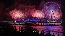 Kembang api menerangi langit selama upacara pembukaan Dubai Eye, yang dikenal sebagai Ain Dubai, di kota Emirat, dekat Dubai Marina, Kamis (21/10/2021). Pembukaan bianglala terbesar di dunia ini dilakukan dengan pesta kembang api serta pertunjukan drone. (Giuseppe CACACE / AFP)