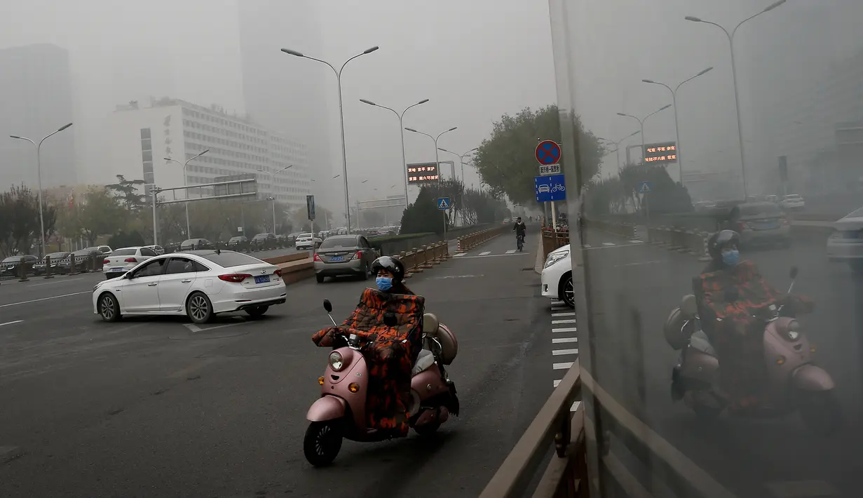 Seorang wanita mengendarai sepeda listrik mengenakan masker di sebuah jalan yang diselimuti kabut asap tebal di Beijing, China (14/11). Pihak berwenang mengeluarkan peringatan kuning untuk polusi udara buruk pada hari Rabu. (AP Photo/Andy Wong)