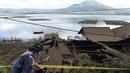 Seorang wanita berjalan melewati rumah-rumah di tepi Danau Batur yang rusak akibat tanah longsor yang dipicu gempa di Bangli, Bali, Sabtu (16/10/2021). Beberapa orang tewas dan lainnya luka-luka saat gempa berkekuatan sedang dan gempa susulan menghantam pulau itu Sabtu dini hari. (AP Photo/Dewa Raka