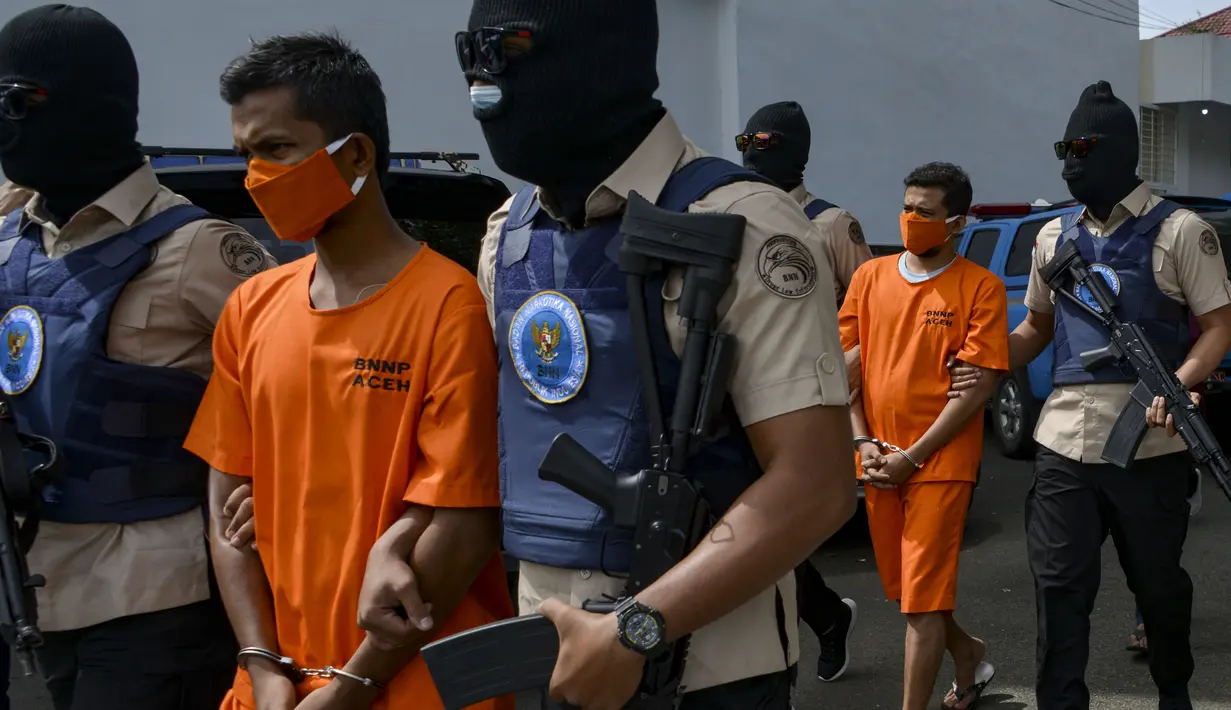 Petugas Badan Narkotika Nasional Indonesia (BNN) mengawal dua pria lokal yang diduga menyelundupkan sabu pada konferensi pers di Banda Aceh (13/10/2020). (AFP Photo/Chaideer Mahyuddin)