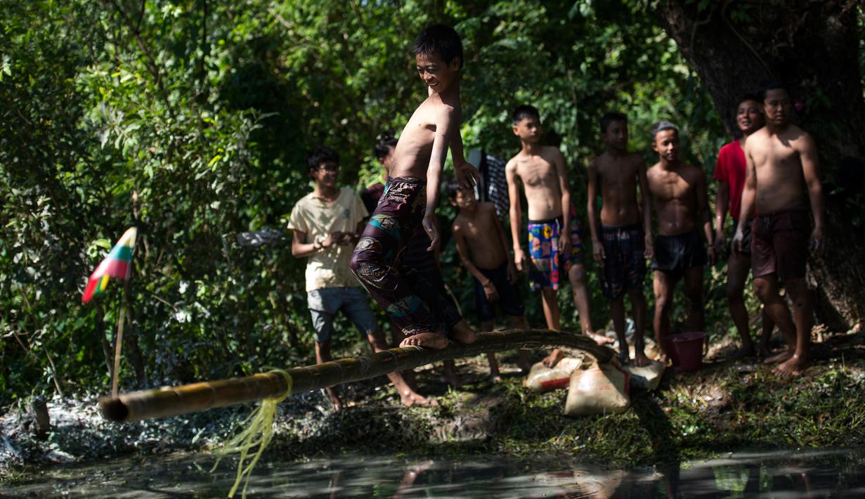 Seorang anak berjalan di atas tiang untuk mencoba meraih bendera nasional memperingati Hari Kemerdekaan Myanmar di pinggiran Yangon (4/1). Myanmar merayakan peringatan ke-71 deklarasi kemerdekaannya dari kolonial Inggris. (AFP Photo/Ye Aung Thu)