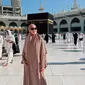 Berpose di depan Ka'bah, Maia tampil memesona dibalut gamis dan hijab syar’i serba warna krem. Penampilannya makin kece dengan aksesori kacamata hitam. [@maiaestiantyreal]