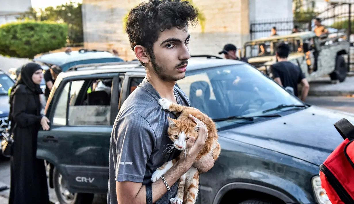 Seorang pemuda memeluk seekor kucing di dadanya saat orang-orang yang melarikan diri dari desa mereka di Lebanon selatan diterima di sebuah lembaga seni yang diubah menjadi tempat penampungan bagi para pengungsi akibat konflik, di Beirut pada 23 September 2024. (FADEL ITANI/AFP)