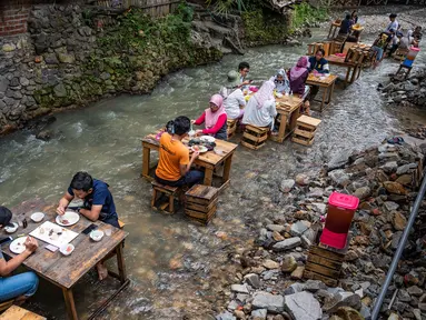 Pelanggan menikmati makan siang di sebuah restoran dengan meja yang berada di tengah aliran sungai di Kampung Kemensah di pinggiran Kuala Lumpur, Malaysia, Selasa (14/7/2020). Tak perlu khawatir, air sungai yang datang dari bukit ini masih bersih dan menyegarkan. (Photo by Mohd RASFAN / AFP)