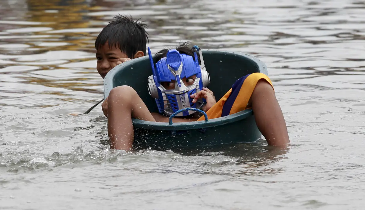 Seorang bocah mendorong rekannya yang menaiki ember menyebrangi jalan yang terendam banjir di Kota Longos, Malabon City, Manila Utara, Senin (6/7/2015). Akibat badai aktivitas penerbangan, pelabuhan dan sekolah-sekolah ditutup. (REUTERS/Romeo Ranoco)