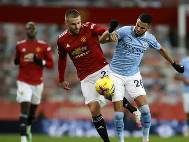 Bek Manchester United, Luke Shaw (kiri), berebut bola dengan striker Manchester City, Riyad Mahrez, dalam laga lanjutan Liga Inggris 2020/21 pekan ke-12 di Old Trafford Stadium, Sabtu (12/12/2020). Manchester United bermain imbang 0-0 dengan Manchester City. (AFP/Phil Noble/Pool)