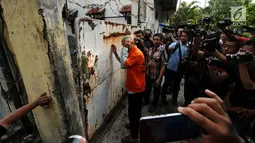 Tersangka penampung TKI Ilegal bersiap masuk ke dalam rumah di Jalan Percetakan Negara X, Jakarta, Rabu (31/5). Bersama satu tersangka, petugas Dirtipidum Mabes Polri melakukan pencarian barang bukti baru. (Liputan6.com/Helmi Fithriansyah)