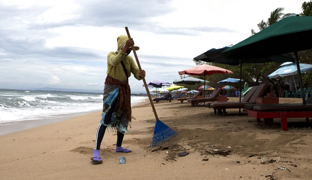 Seorang wanita menyapu sampah di Pantai Kuta, Bali, Jumat (4/2/2022). Bali kembali dibuka untuk pelancong asing dari semua negara setelah penerbangan internasional dilanjutkan untuk pertama kalinya dalam dua tahun, tapi pengunjung tetap wajib karantina. (AP Photo/Firdia Lisnawati)