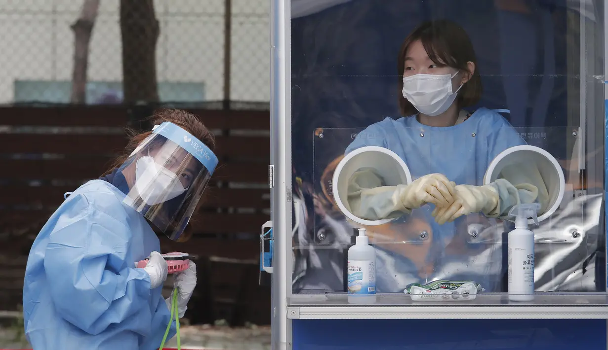 Seorang pekerja medis memegang kipas angin portabel selama panas terik sementara petugas polisi menjalani tes COVID-19 di klinik darurat di Badan Kepolisian Metropolitan Seoul di Seoul, Korea Selatan, Rabu, (19/8/2020). (AP Photo / Ahn Young -joon)