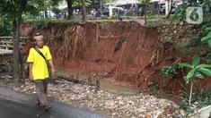 Warga berjalan dekat dinding Kali Baru yang longsor di Jalan Raya Bogor, Kramat Jati, Jakarta Timur, Jumat (10/1/2020). Longsor yang terjadi akibat banjir beberapa waktu lalu itu berpotensi menyebabkan longsor susulan akibat tidak adanya turap penahan dinding kali. (Liputan6.com/Immanuel Antonius)