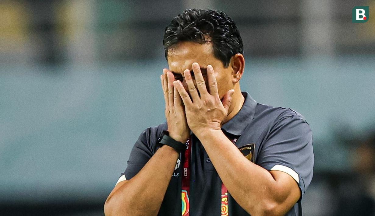 Pelatih kepala Timnas Indonesia U-17, Bima Sakti, menutup wajahnya saat anak asuhnya digempur pemain Timnas Ekuador U-17 pada laga pertama Grup A Piala Dunia U-17 di Stadion Gelora Bung Tomo, Surabaya, Jumat (10/11/2023) malam WIB. Kedua tim bermain sama kuat 1-1. (Bola.com/Bagaskara Lazuardi)