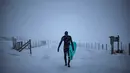 Seorang surfer atau peselancar berjalan keluar dari air membawa papannya di bawah hujan salju di Unstad, Norwegia Utara (11/3). (AFP Photo/Olivier Morin)