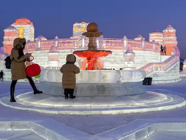Pengunjung mengamati pahatan es yang dihiasi sorotan lampu warna-warni di Festival Dunia Es dan Salju Harbin, Harbin, Provinsi Heilongjiang, China, Selasa (5/1/2021). Festival yang berlangsung tahunan ini adalah festival salju dan es terbesar di dunia. (Chinatopix via AP)