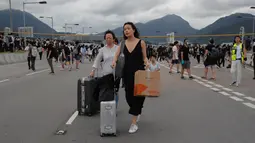 Penumpang berjalan kaki ke bandara ketika pemrotes pro-demokrasi memblokir jalan di luar bandara di Hong Kong (1/9/2019). Demonstran pro-demokrasi penentang RUU Ekstradisi kembali menjadikan bandara sebagai tempat aksi demo. (AP Photo/Kin Cheung)