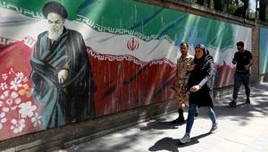 Pejalan kaki melewati lukisan mural yang menggambarkan pendiri Republik Islam Iran Ayatollah Ruhollah Khomeini dan bendera nasional di sepanjang dinding bekas Kedutaan Amerika Serikat (AS) di Ibu Kota Teheran, Iran, Sabtu (22/6/2019). (ATTA KENARE/AFP)