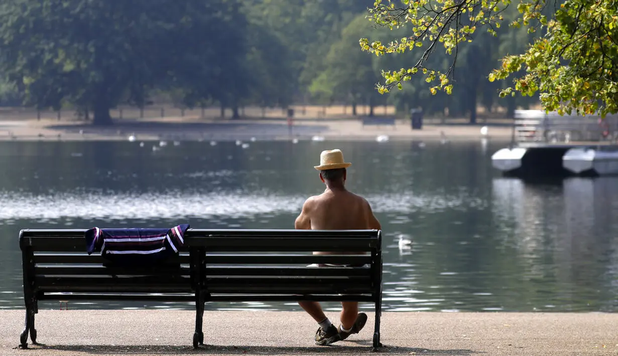 Seorang pria duduk di bangku menikmati suasana sungai Serpentine di Hyde Park di London, Rabu, (12/8/2020). Peringatan badai masih berlaku untuk sebagian besar Inggris pada hari Rabu, sementara suhu tinggi diperkirakan lagi di banyak bagian Inggris. ( AP Photo / Kirsty Wigglesworth)