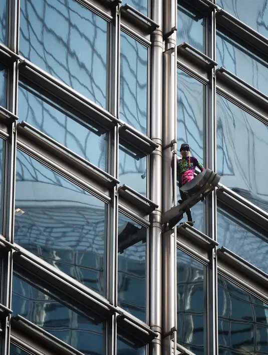 Alain Robert yang dijuluki 'French Spiderman' memanjat gedung pencakar langit Cheung Kong Center di Hong Kong, Jumat (16/8/2019). Selama pendakian, Alain Robert memasang spanduk yang menampilkan bendera Hong Kong dan China. (Lillian SUWANRUMPHA/AFP)