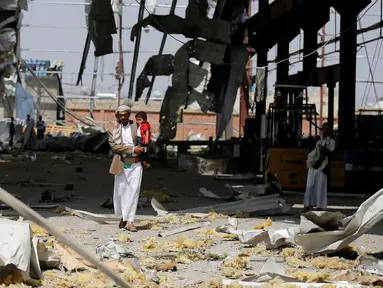 Seorang pria menggendong anaknya di sebuah bangunan pabrik pipa dan pompa air yang hancur akibat serangan udara Arab Saudi di Sanaa, Yaman, Kamis (15/9). Dalam serangan ini tidak ada korban jiwa. (REUTERS/Khaled Abdullah)