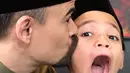 Suami Bunga Citra Lestari, Ashraf Sinclair mencium putranya Noah Aidan Sinclair saat berpose dengan mengenakan busana serasi dan peci hitam. (Instagram/@ashrafsinclair)