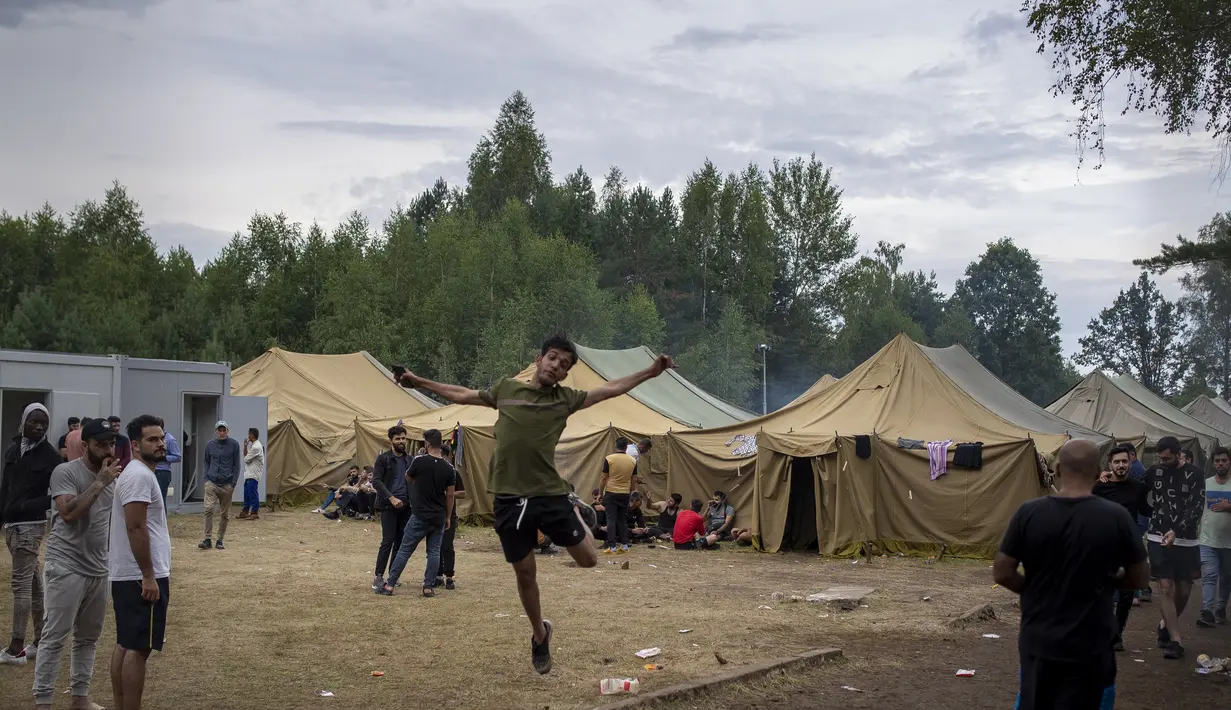 Seorang migran melompat ketika yang lain berjalan di dalam kamp pengungsi yang baru dibangun di tempat latihan militer Rudninkai, sekitar 38 km (23,6 mil) selatan dari Vilnius, Lithuania, Rabu (4/8/2021). (AP Photo/Mindaugas Kulbis)