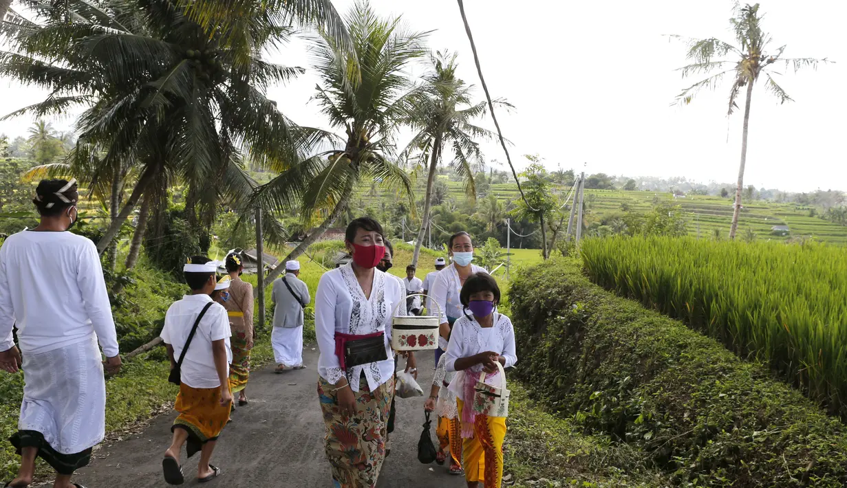 Orang-orang yang memakai masker wajah sebagai pencegahan terhadap wabah virus Corona berjalan ke sebuah pura di sebuah desa di Bali, Senin (21/9/2020). (AP Photo / Firdia Lisnawati)