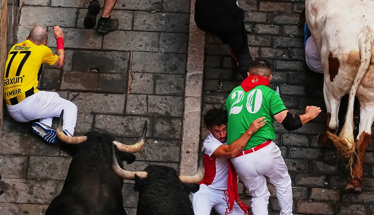 Pengunjung festival terjatuh di depan banteng-banteng aduan Victoriano del Río saat acara lari banteng ketiga di festival San Fermín di Pamplona, Spanyol, Kamis, 9 Juli 2026. (AP Photo/Miguel Oses)