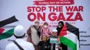 Pengunjuk rasa berfoto dengan latar belakang pesan yang menyerukan diakhirinya perang di Gaza dalam aksi unjuk rasa untuk mendukung Palestina di luar Kedutaan Besar Amerika Serikat di Jakarta, Indonesia, Sabtu13 Januari 2024. (AP Photo/Dita Alangkara)