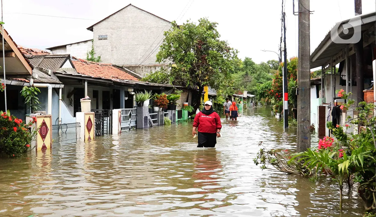 Warga melintasi genangan air di salah satu permukiman di kawasan Cakung, Jakarta Timur, Rabu (29/1/2025). (Liputan6.com/Herman Zakharia)