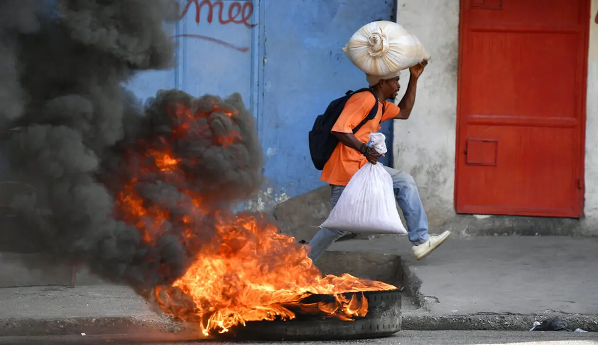 Seorang pria berlari melewati ban yang dibakar oleh pengunjuk rasa yang kesal dengan meningkatnya kekerasan di lingkungan Lalue, Port-au-Prince, Haiti, Rabu (14/7/2021). Presiden Haiti Jovenel Moise dibunuh pada 7 Juli. ( AP Photo/Fernando Llano)