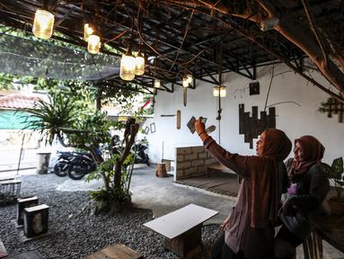 Pengunjung berswafoto di Kedai Poci (KEPO), Hj Kelik, Kelapa Dua Srengseng, Jakarta Barat, Sabtu (18/9/2021). Pemilik usaha kafe ini keluhkan sepi dikarenakan baru bisa membuka usahanya belum lama ini. (Liputan6.com/Johan Tallo)