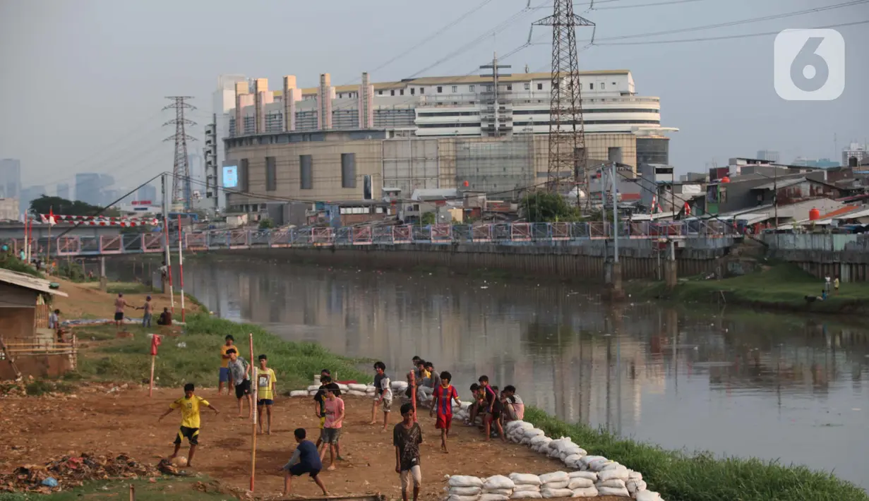 Sejumlah anak bermain sepak bola di sebuah lahan kosong di Pinggir Banjir Kanal Barat, Jakarta, Selasa (12/10/2021). Alih fungsi lahan menjadi kawasan hunian dan perkantoran mengakibatkan semakin minimnya lahan bermain bola bagi anak di Ibu kota.  (Liputan6.com/Johan Tallo)